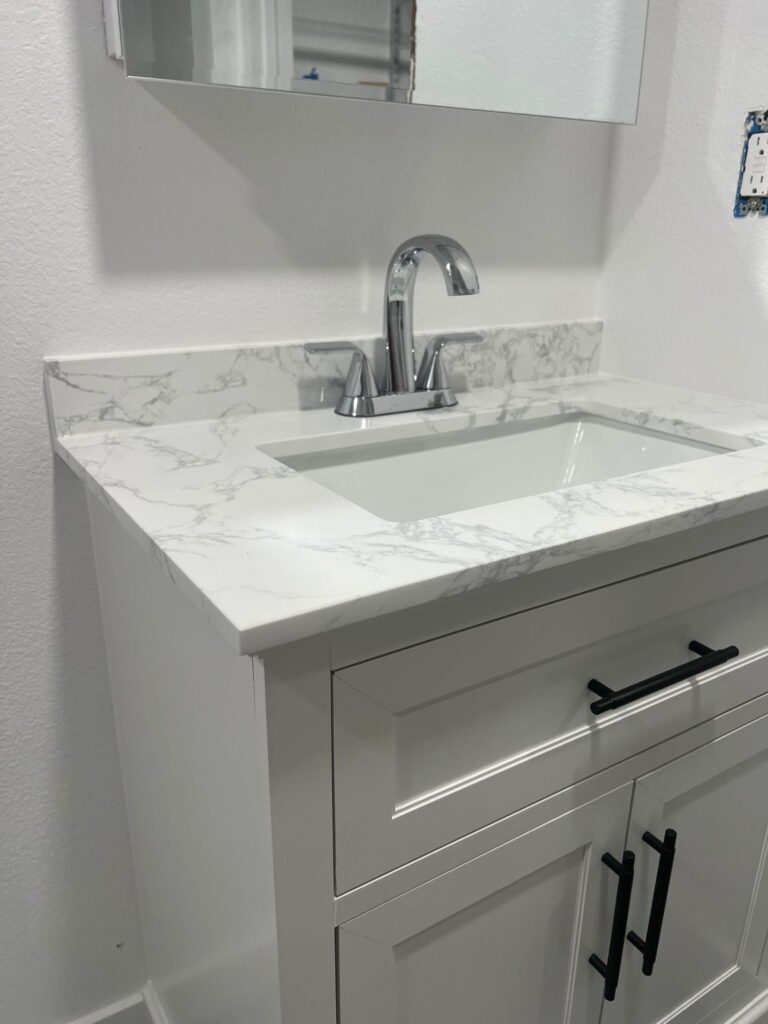 A white vanity with a marble-patterned top, a sink, and black handles.