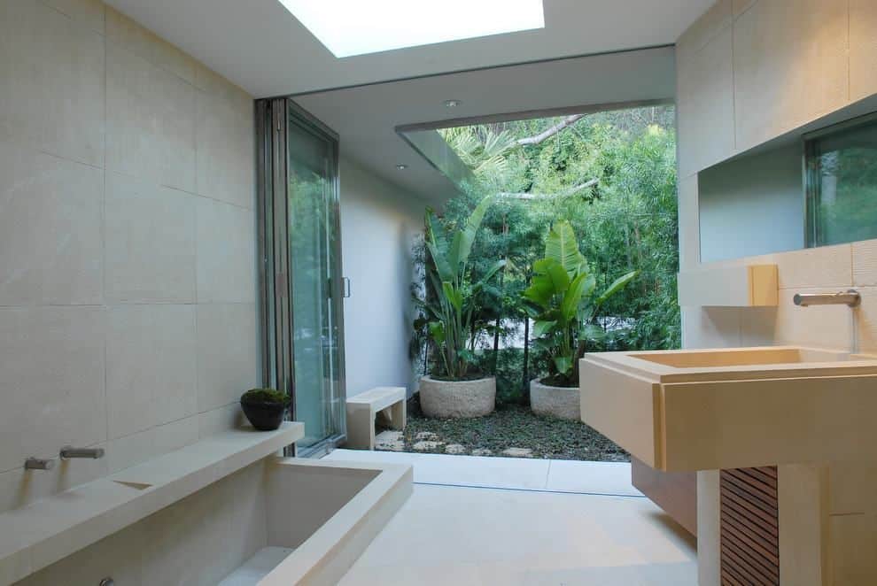 A modern bathroom with a natural stone vanity, a built-in tub, and an open-air plant atrium