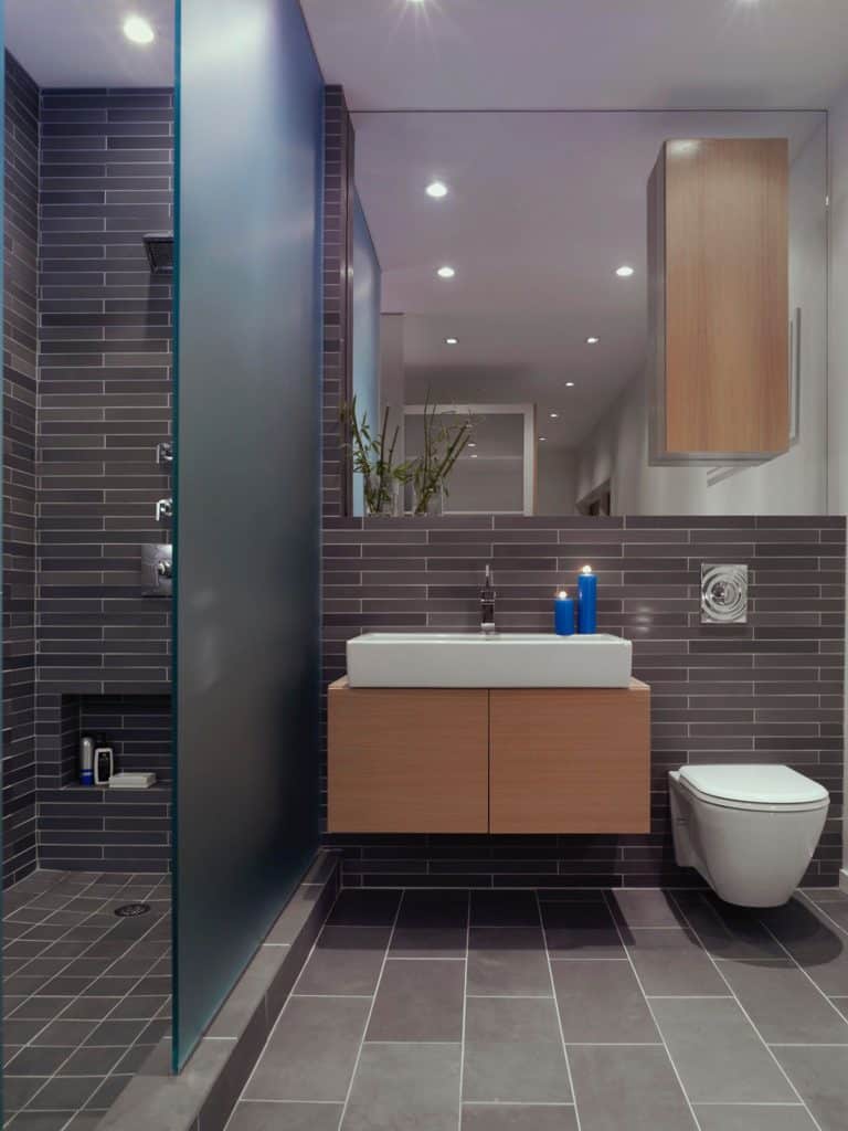 A modern gray bathroom with a wood vanity and glass shower panel