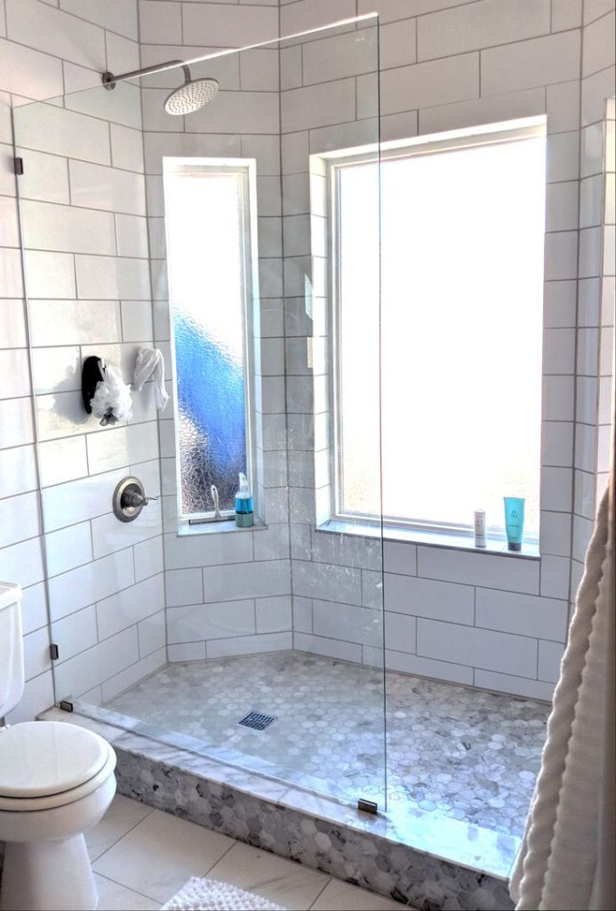 A white subway tile shower with a glass door and a hexagon floor.